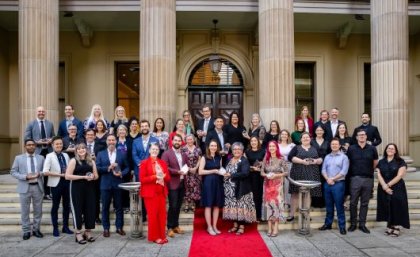 A group of UQ researchers holding award trophies standing out the front of a sandstone building on a red carpet